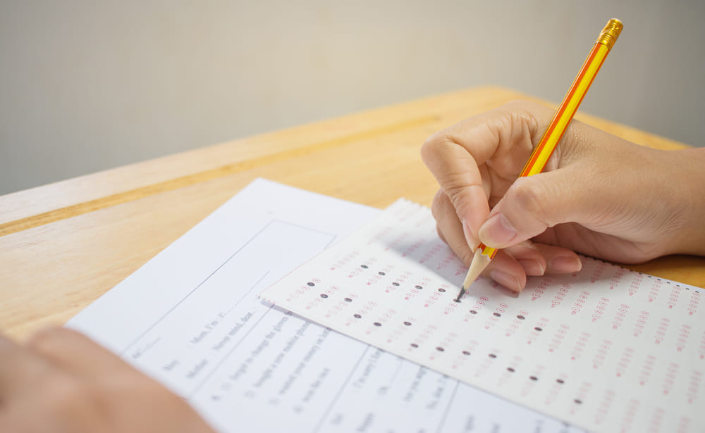 Mão preenchendo cartão-resposta de múltipla escolha com lápis durante simulado.
