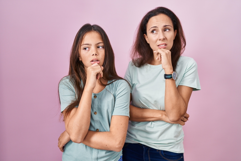 mãe e filha de cerca de 10 anos pensativas, com a mão no queixo e expressão de dúvida.