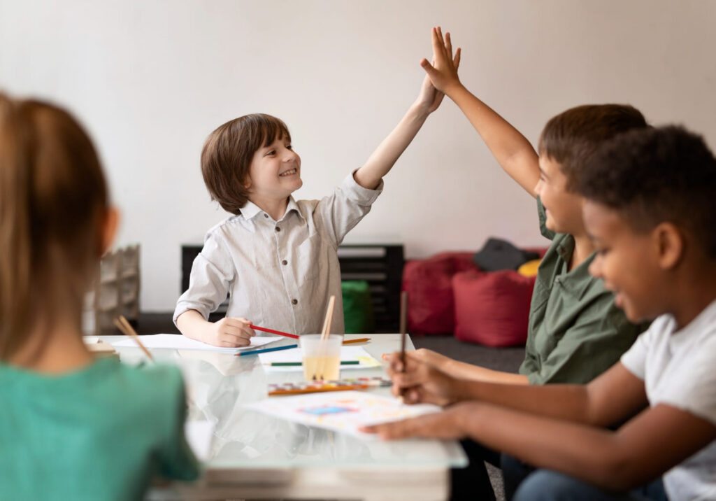 Crianças colaborando e trocando um high five, prática de educação socioemocional em sala de aula.