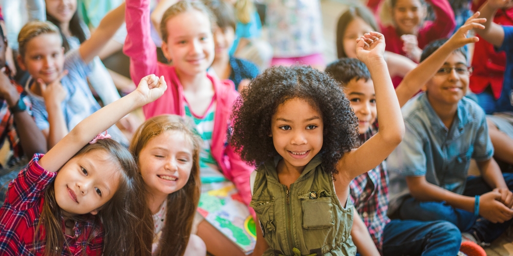 grupo de crianças de 6 a 8 anos levantando as mãos e sorrindo.