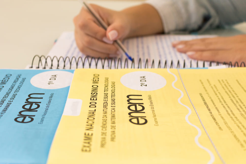 Cadernos do Enem com estudante escrevendo anotações durante os estudos.