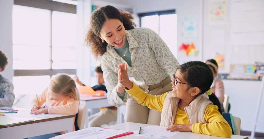 Professora fazendo "high-five" com aluna comemorando sua evolução na aprendizagem.