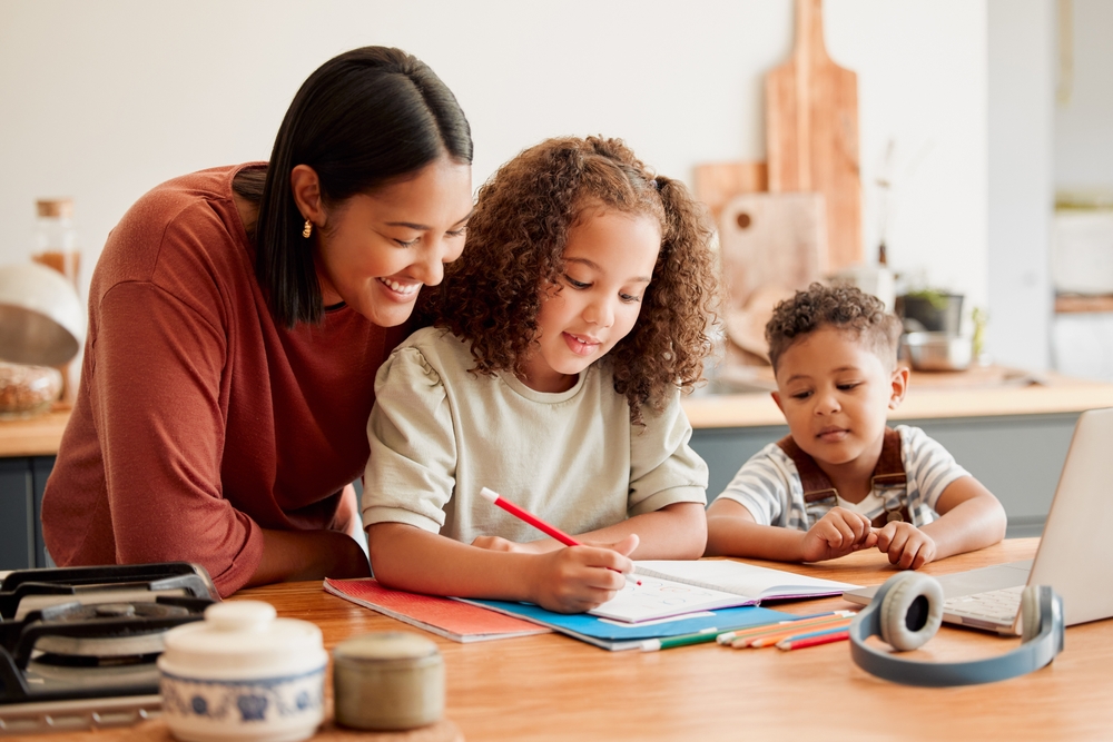 Mãe acompanhando o estudo dos filhos pequenos em casa, representando o conceito de homeschooling.