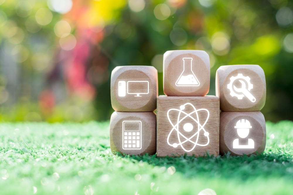 Blocos de madeira com ícones de ciência, tecnologia, engenharia e matemática, ilustrando a interdisciplinaridade.