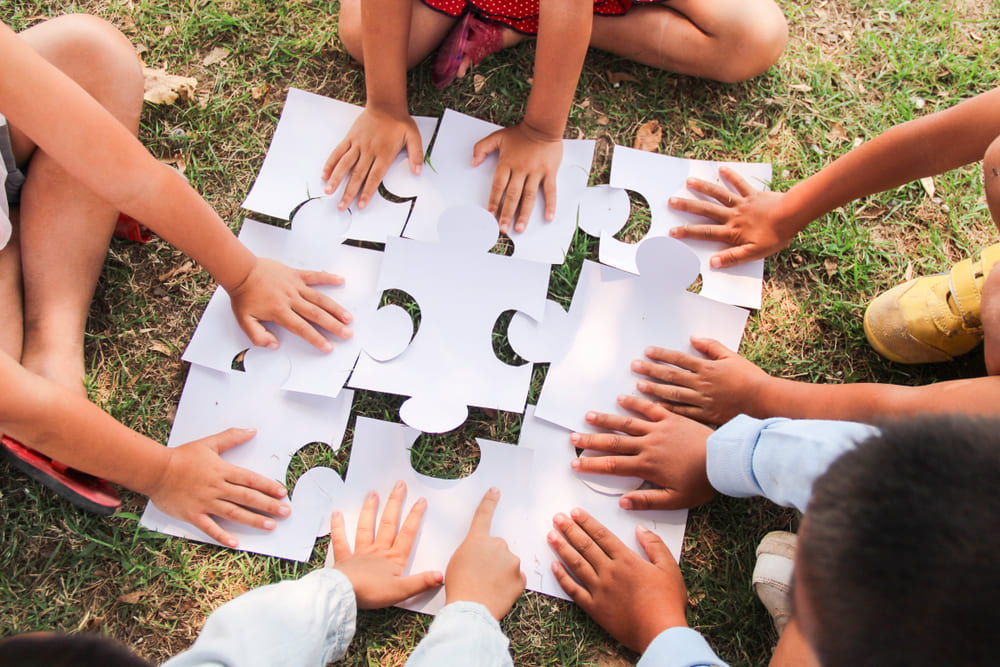 Crianças aplicando o método Freinet em atividade de cooperação ao montar um quebra-cabeça coletivo.