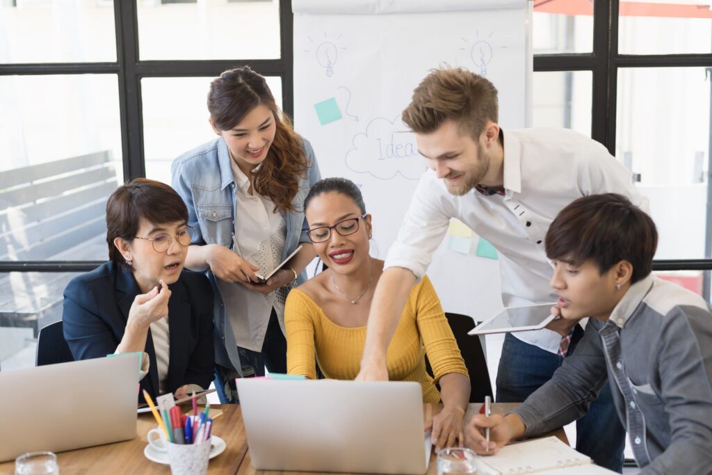 Equipe reunida em frente ao computador trabalhando de forma colaborativa, exemplo da gestão democrática da escola.