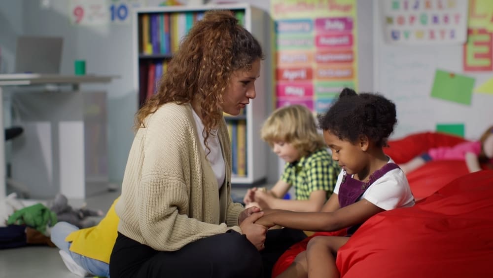 Professora conversa com aluna de maneira empática em sala de aula, reforçando práticas sobre como prevenir o bullying na escola.