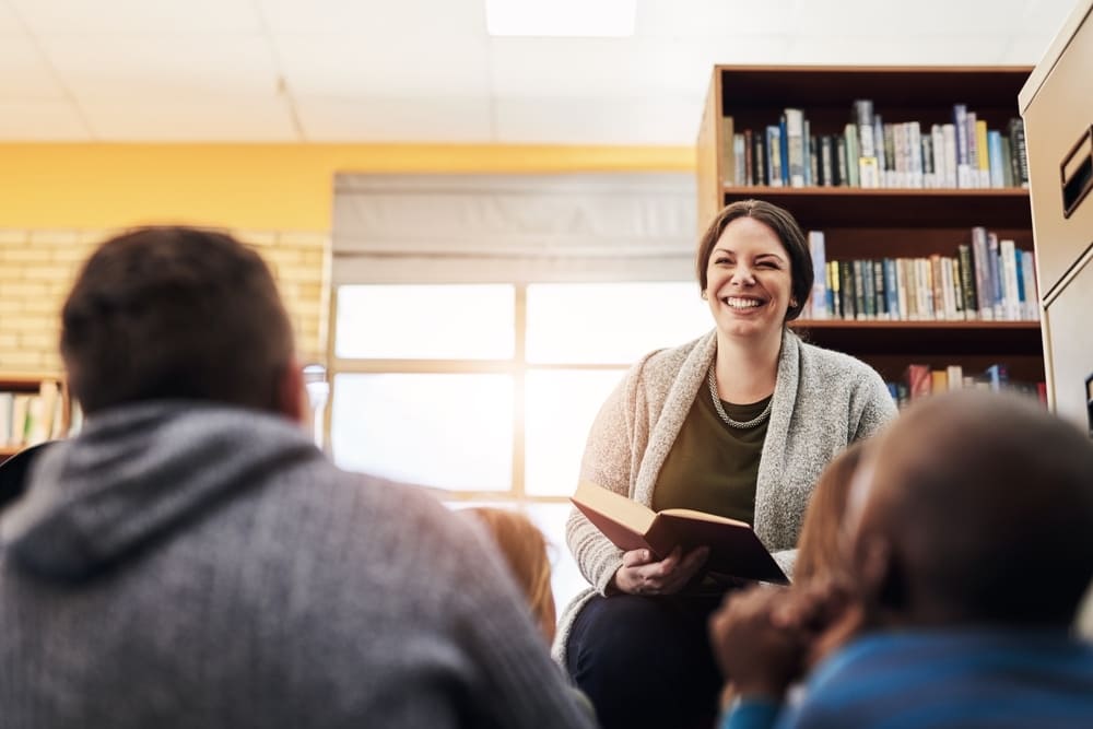 Pedagoga lendo um livro para crianças em uma biblioteca escolar no Dia da Pedagoga.