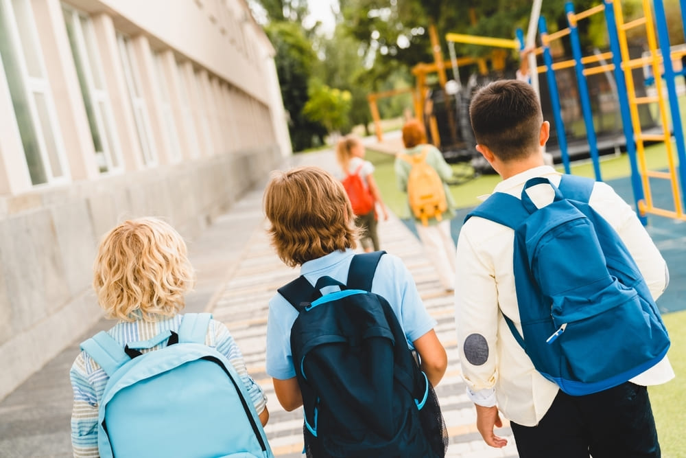 Crianças caminhando com mochilas para escola no primeiro dia de aula.