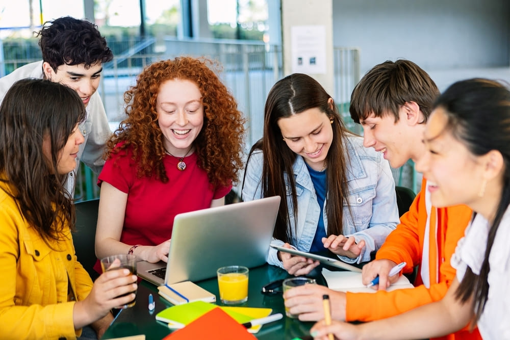 Estudantes trabalhando em grupo usando tecnologia, aplicando o método PBL para resolver problemas de forma colaborativa.
