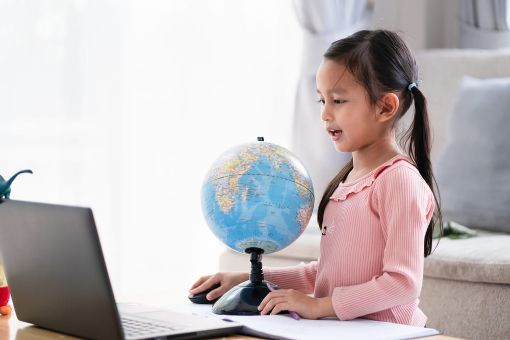 Criança interagindo com um globo terrestre e computador, simbolizando o aprendizado no contexto de programa bilíngue e inovações educacionais apresentadas na Bett Brasil.