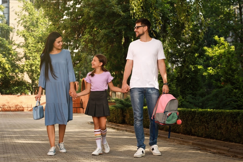 Pais caminhando com sua filha até a escola, demonstrando a importância da presença e envolvimento dos pais na escola.