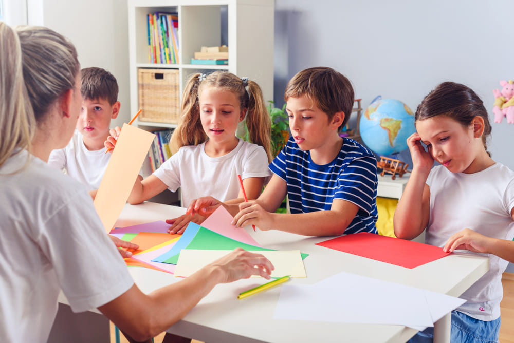 Crianças realizando atividade artística com papéis coloridos em sala de aula durante um projeto cultural.