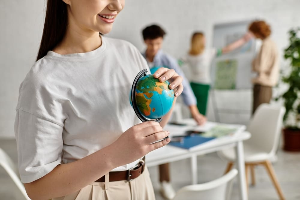 Jovem mulher segurando um globo terrestre em sala de aula, destacando o ensino de Objetivos de Desenvolvimento Sustentável (ODS) em ambiente colaborativo.