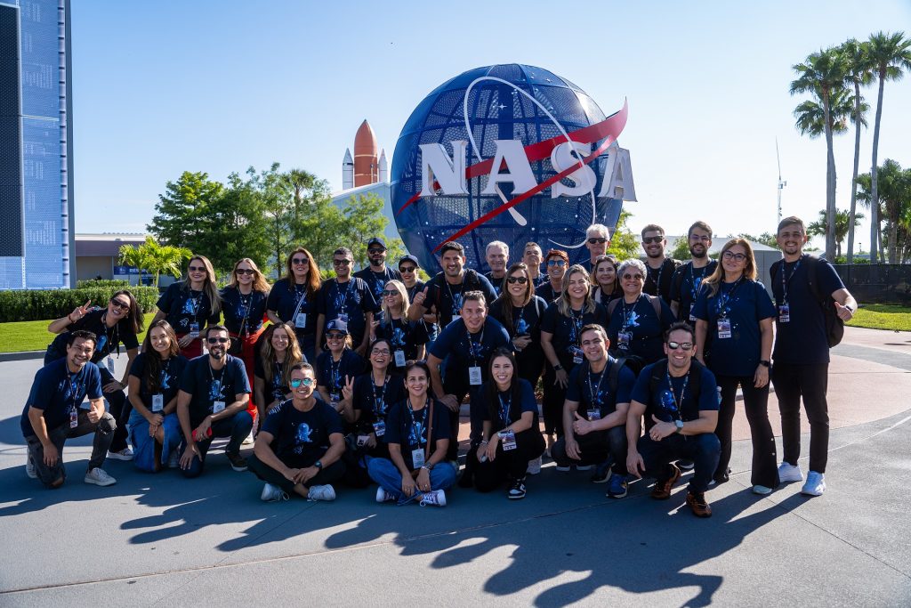 Estudantes e gestores escolares posam em grupo para foto em frente a logo da NASA no Kennedy Space Center