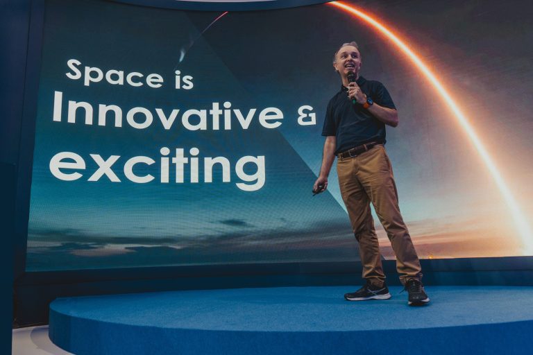Jeff Michaelis em frente a um telão com os dizeres "Space is innovating and exciting"