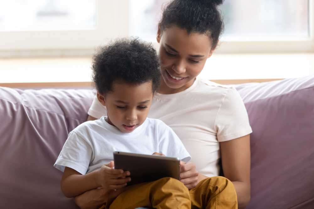 Mãe sentada no sofá com filho no colo usam tablet juntos