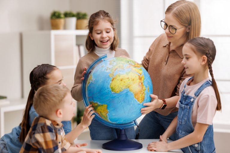 Professora com crianças ao redor de um globo do planeta Terra.