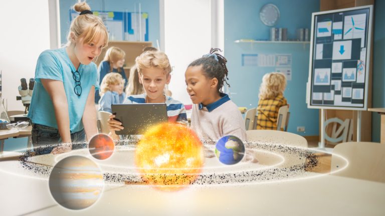 Crianças em sala de aula usam um tablet para descobrir o sistema solar. O Sol e alguns planetas se materializam diante deles.