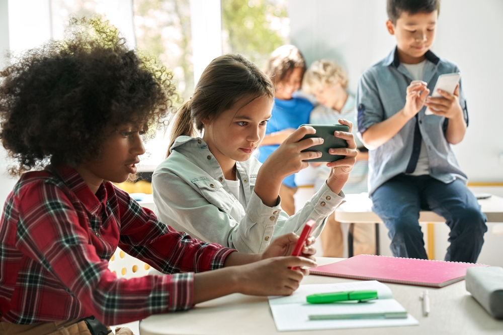 Jovens estudantes usando celular na sala de aula, individualmente.