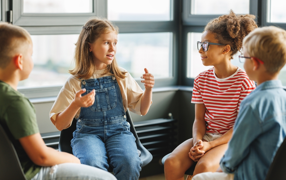 crianças conversam sobre emoções sentados em roda dentro de uma sala de aula