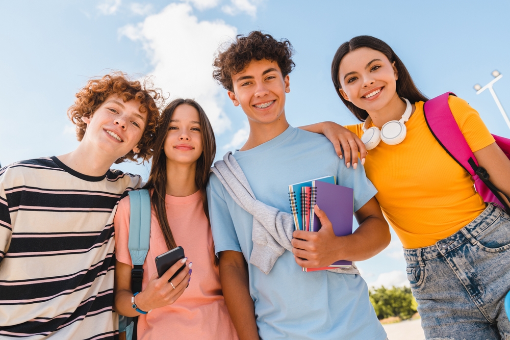 Quatro alunos do Ensino Médio sorriem para foto ao ar livre em dia ensolarado