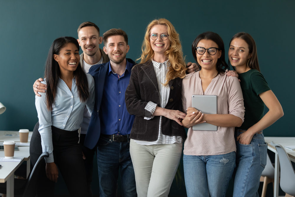 Grupo de professores e professores posa para foto em frente ao quadro de giz, sorrindo.