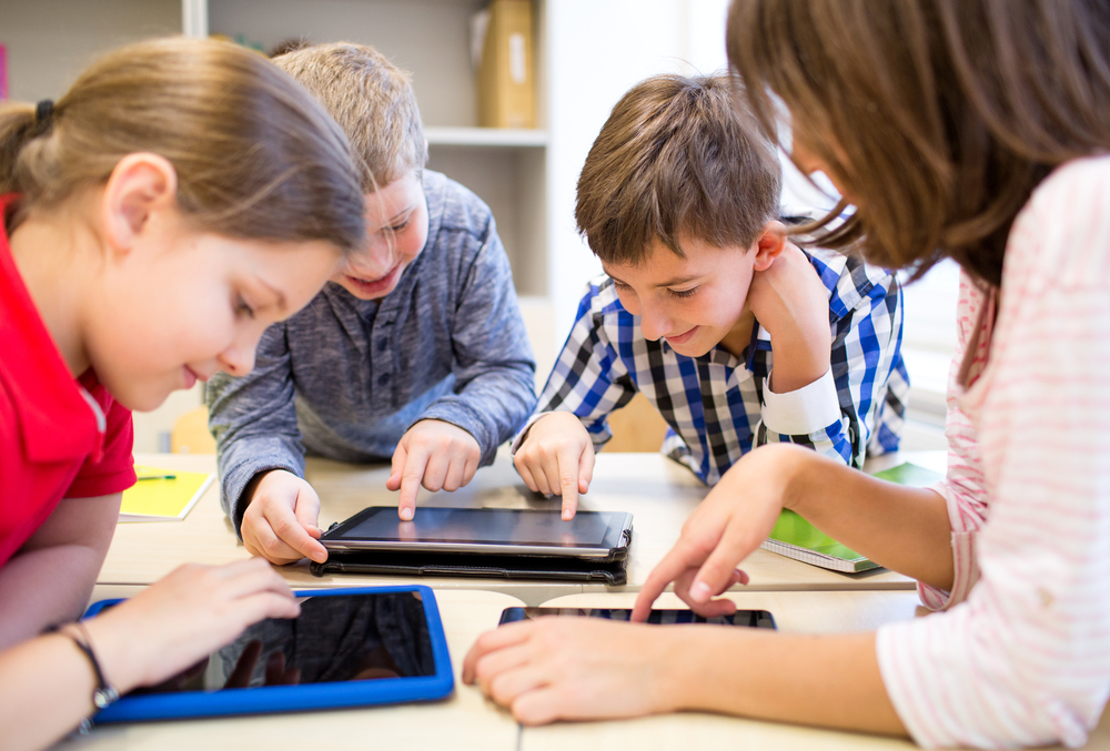 Crianças usam tablets ao redor de uma mesa na escola