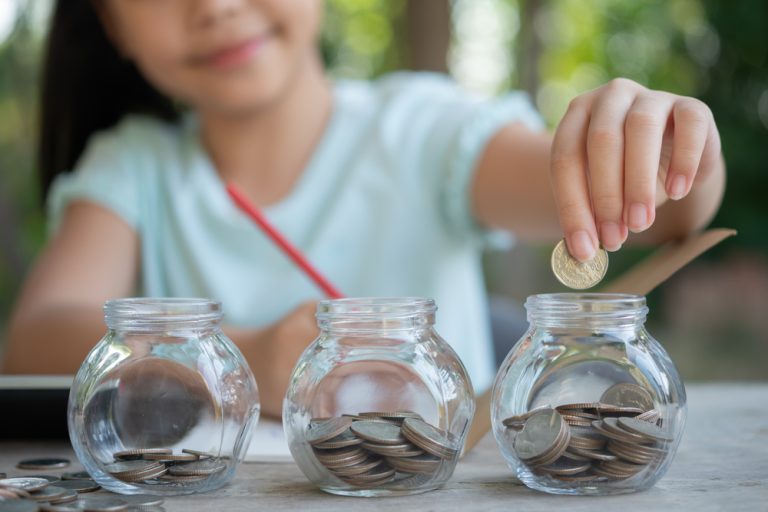 criança guardando moedas em três potinhos de vidro