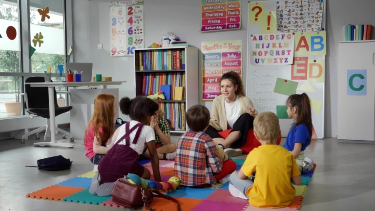 Crianças da Educação Infantil sentam em roda, no chão, junto com a professora.