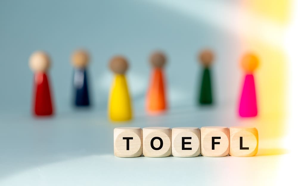 Cubos com a palavra TOEFL em destaque e figuras coloridas ao fundo.