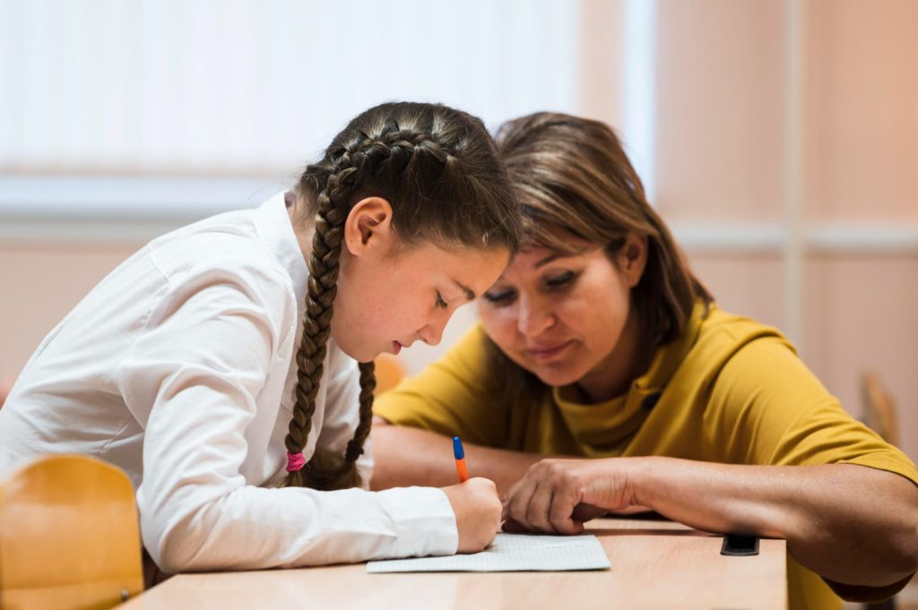 Criança com dificuldades de aprendizagem recebendo apoio de professora durante a atividade escolar.