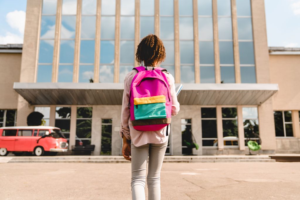 Jovem estudante caminhando em direção à escola, simbolizando a importância da permanência na educação para combater a evasão escolar.