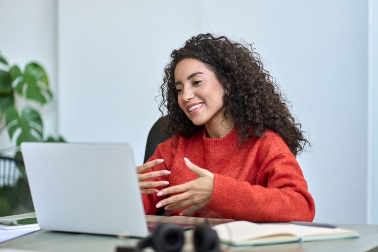 Mulher participando de aula híbrida, comunicando-se em frente a um notebook.
