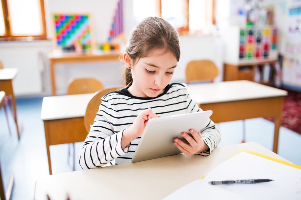 Jovem aluna usando um tablet em sala de aula, representando a importância da inclusão digital na educação.