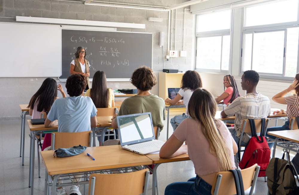 Professora explicando física para alunos em sala de aula, aplicando metodologia no plano de aula com recursos digitais.