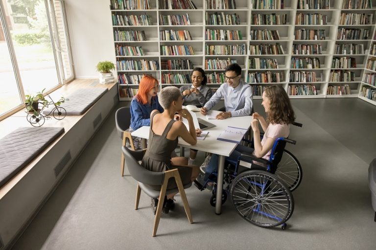 Vista aérea de estudantes em sala de aula, incluindo uma aluna em cadeira de rodas, participando das atividades escolares, representando acessibilidade escolar.