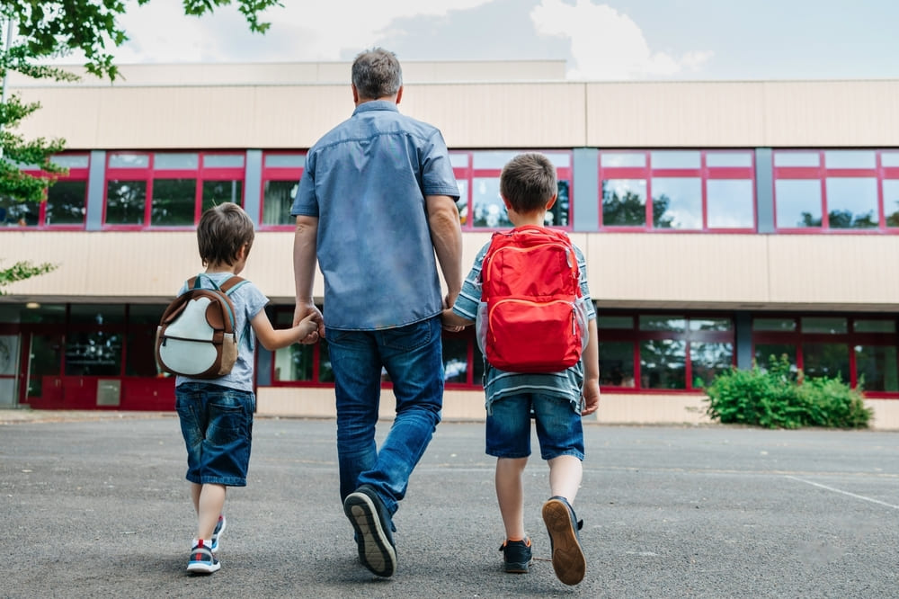 Pai levando seus filhos para o colégio, representando a integração entre família e escola, fator importante na realização de atividades lúdicas sobre família na Educação Infantil.