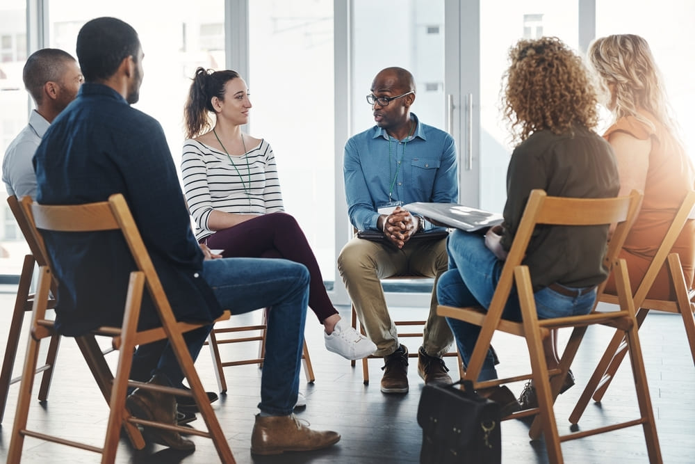 Dinâmica para reunião de pais com seis adultos sentados em círculo, discutindo em um ambiente claro e iluminado.