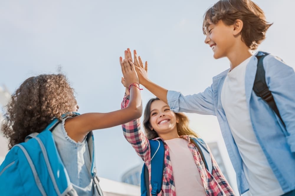 Crianças fazendo high five, sorrindo e se divertindo no retorno às aulas.