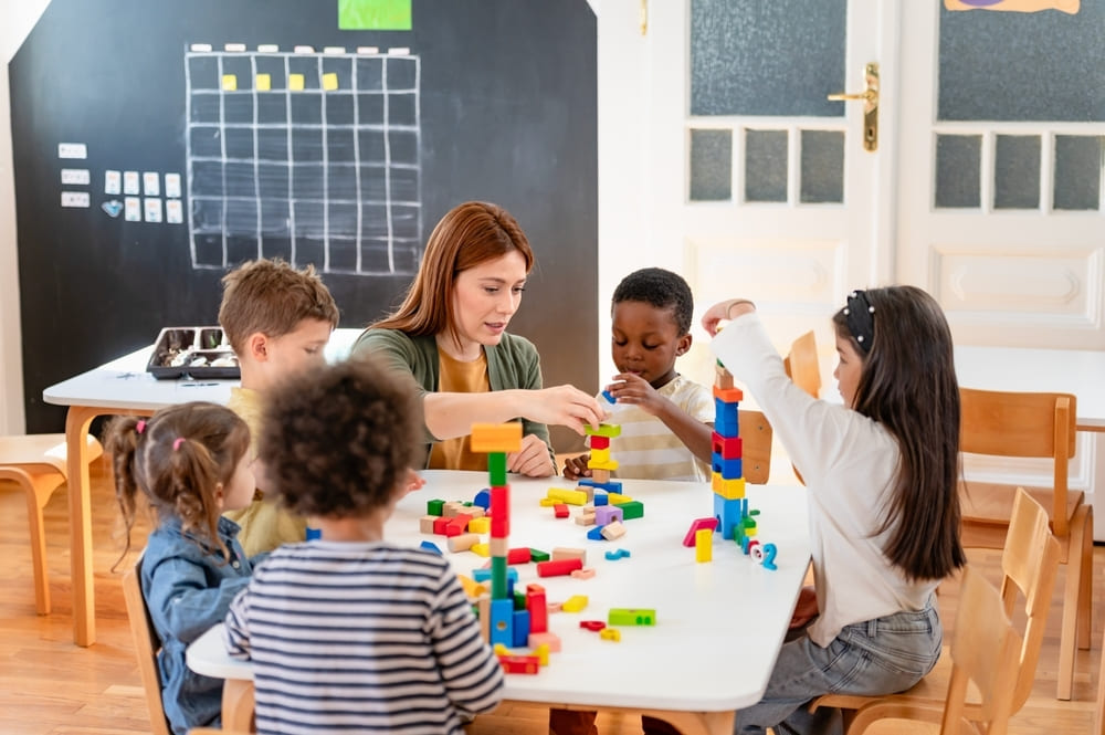 Professora orienta crianças em atividade com blocos de montar dentro de um plano de aula para Educação Infantil.
