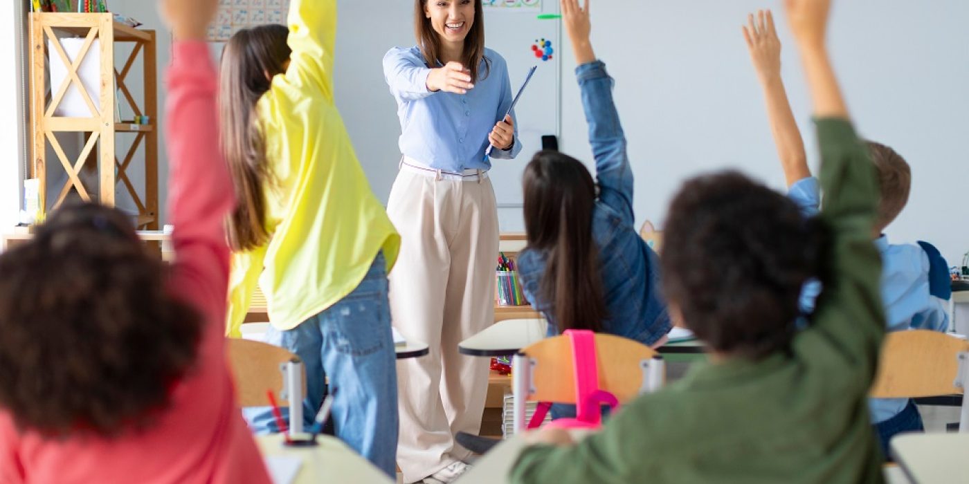 Alunos levantando as mãos em sala de aula multicultural durante dinâmica pedagógica interativa
