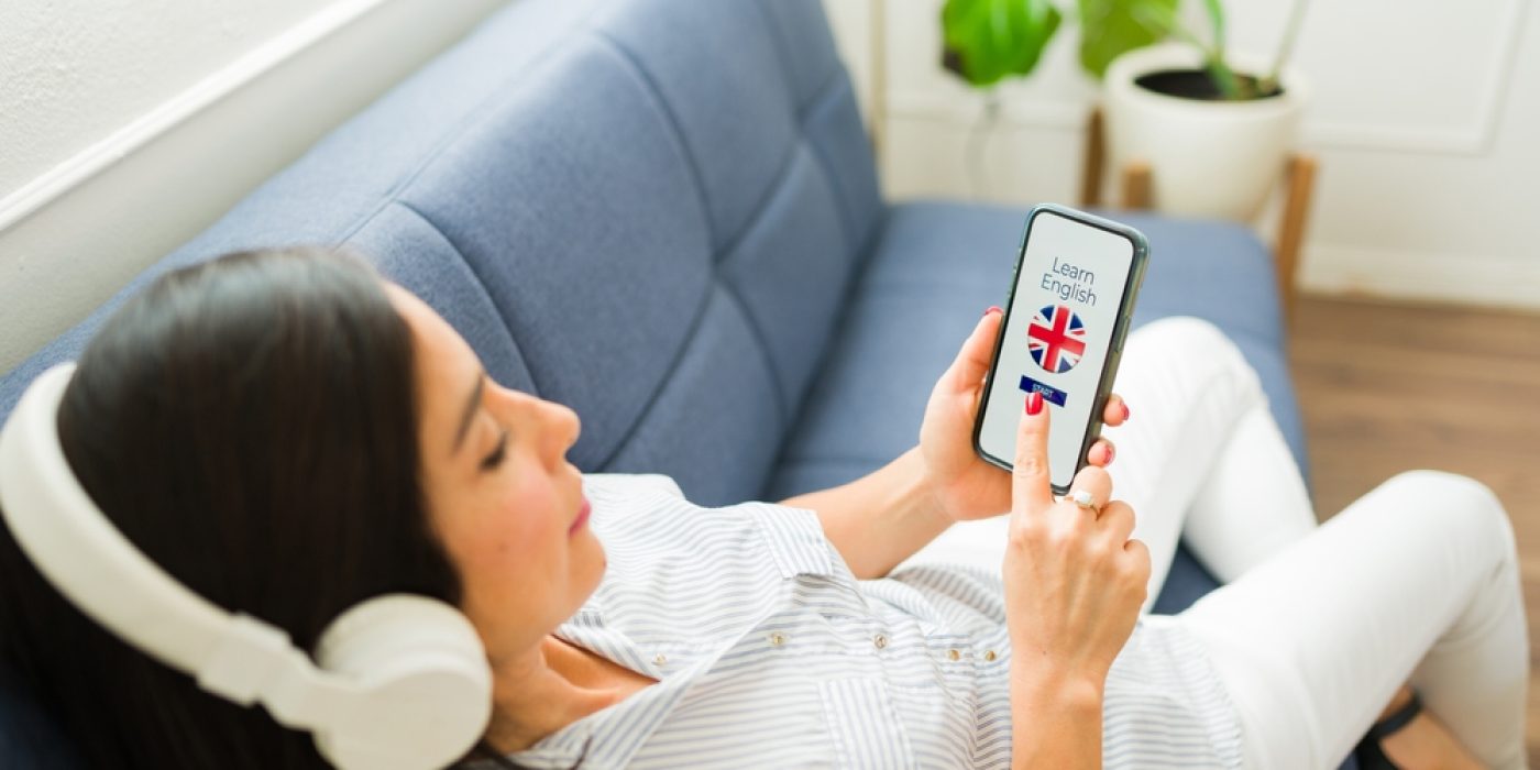 Mulher com fones de ouvido usando aplicativo no celular para aprender inglês.
