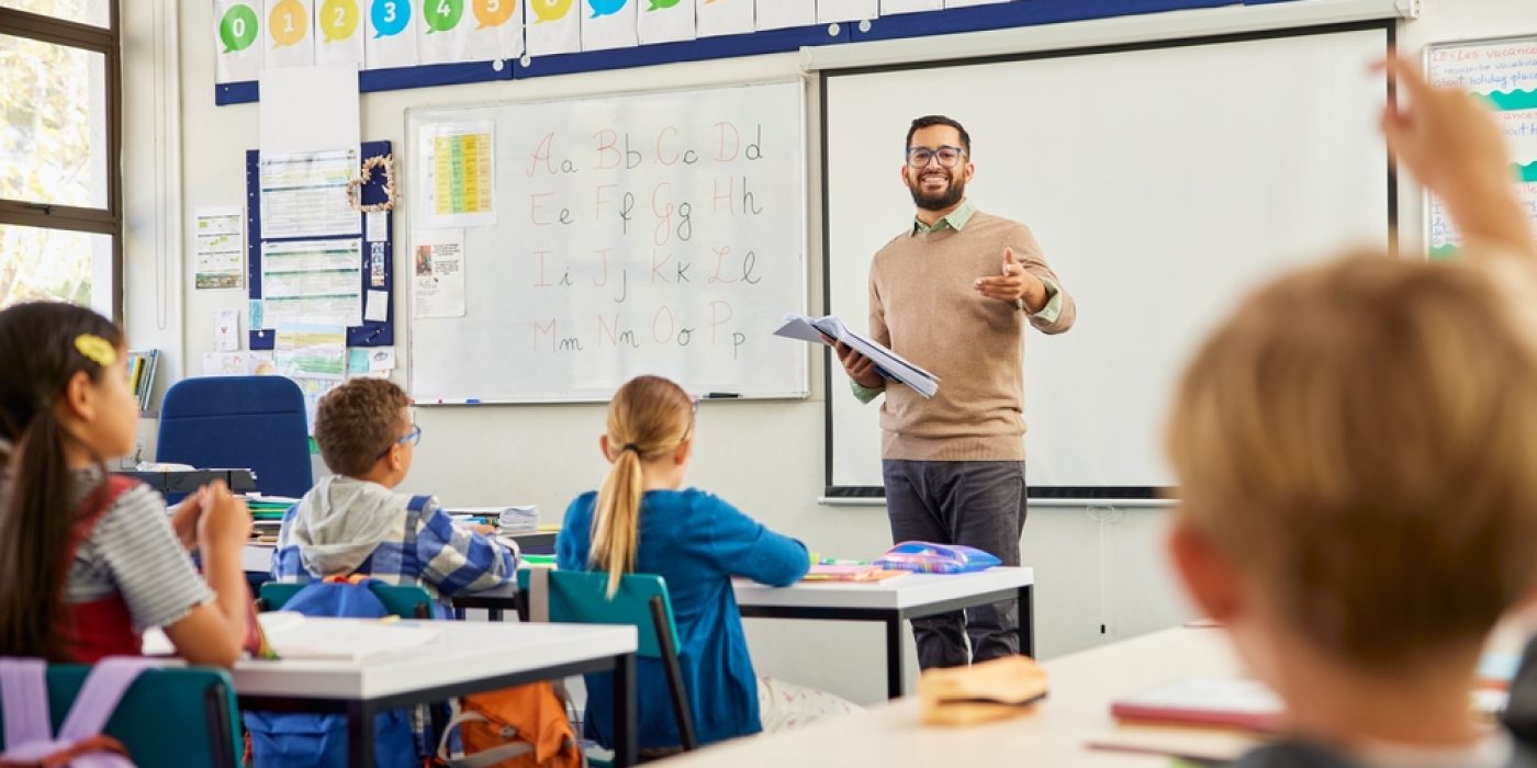 Professor ensina alfabeto em sala de aula para crianças do Ensino Fundamental, em ambiente escolar colorido e interativo.