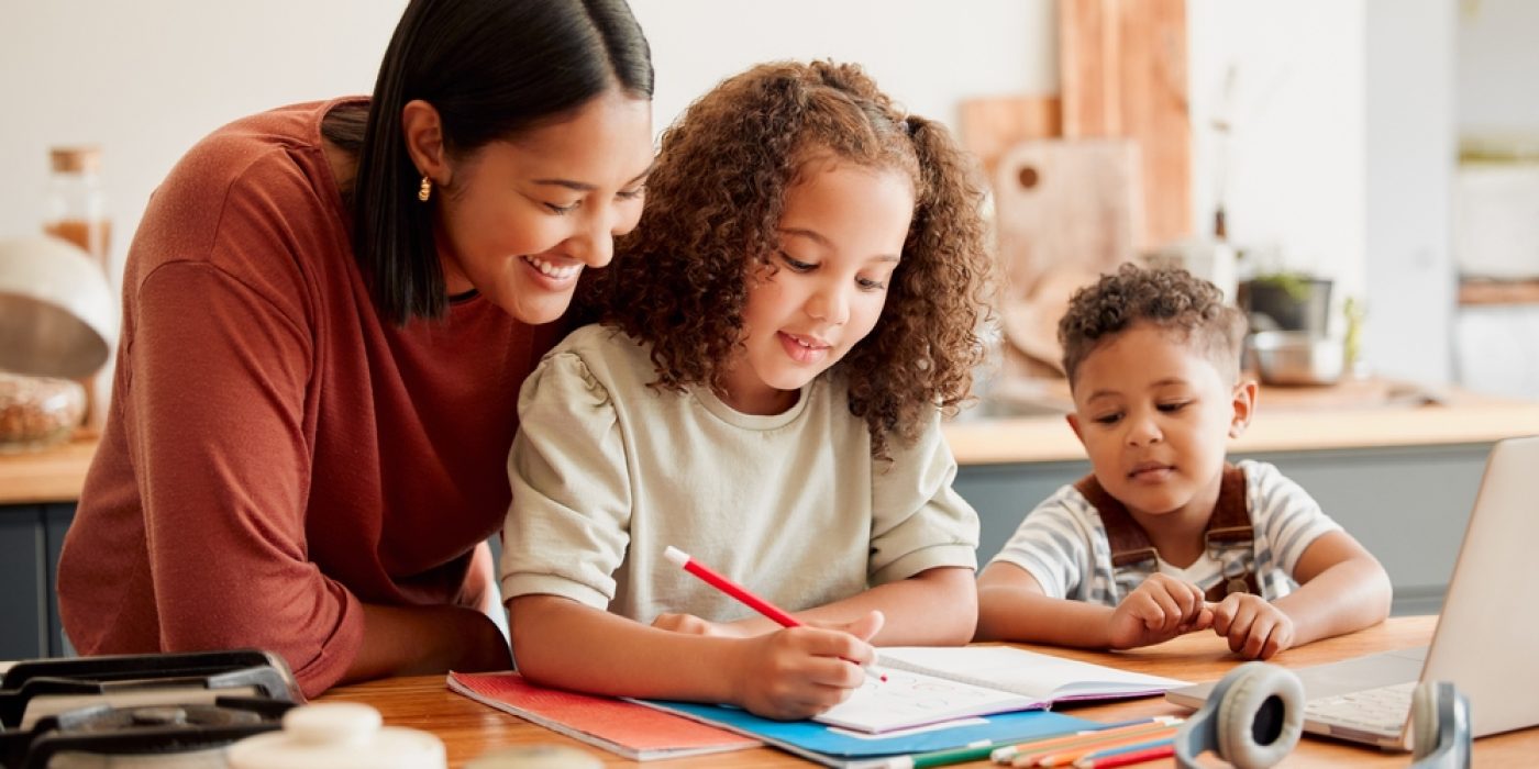 Mãe acompanhando o estudo dos filhos pequenos em casa, representando o conceito de homeschooling.