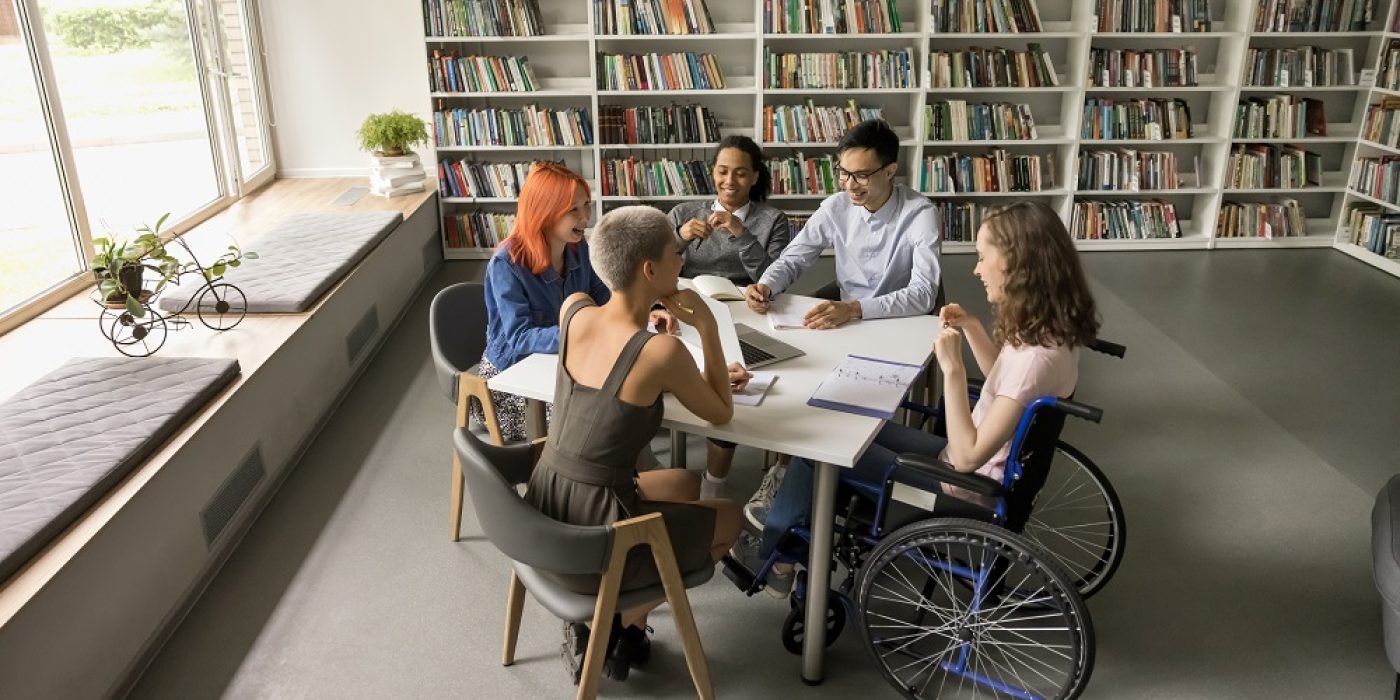 Vista aérea de estudantes em sala de aula, incluindo uma aluna em cadeira de rodas, participando das atividades escolares, representando acessibilidade escolar.