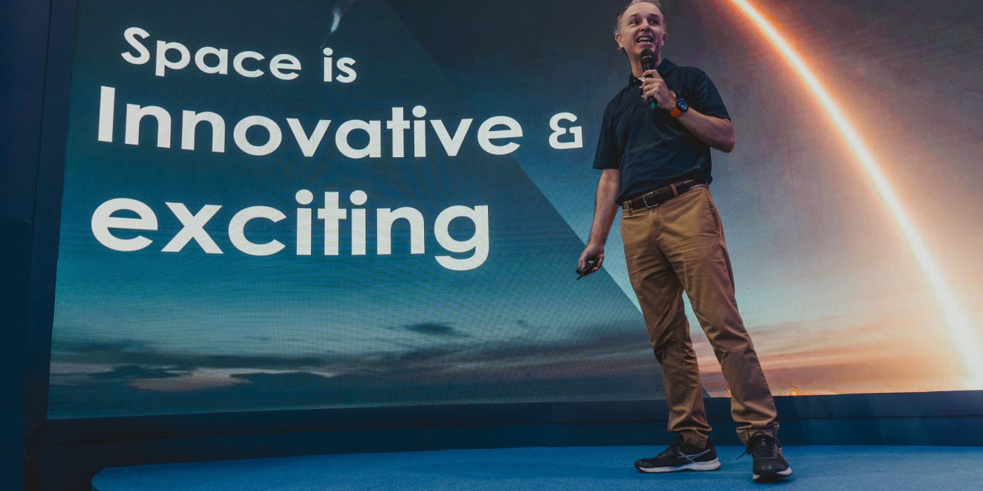 Jeff Michaelis em frente a um telão com os dizeres "Space is innovating and exciting"