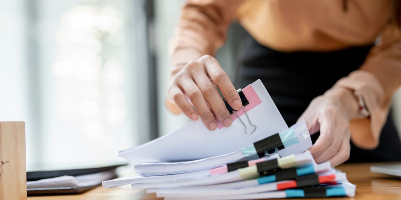 Pessoa organizando pilhas de documentos em mesa de trabalho, representando a gestão financeira escolar.