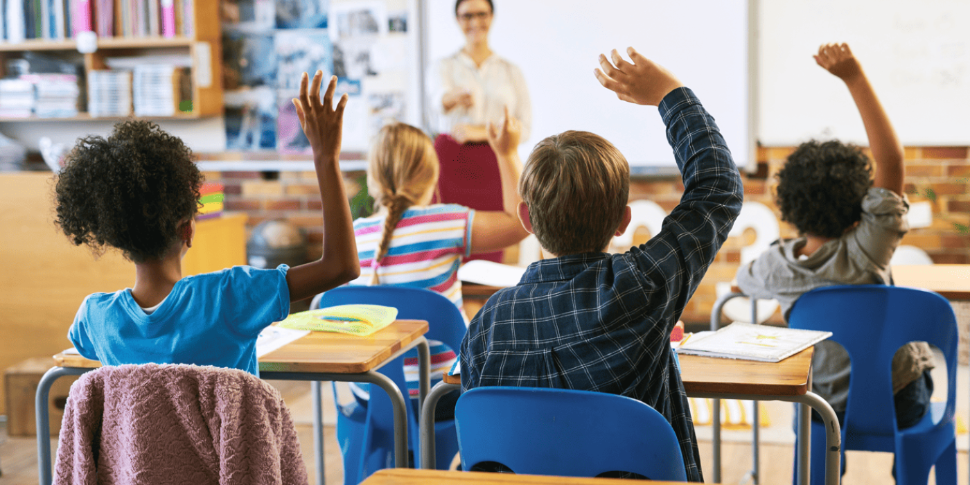 Crianças levantando a mão em sala de aula para responder, seguindo as regras na sala de aula de respeito e participação.