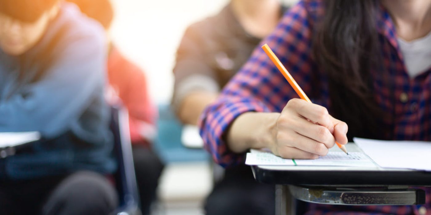 shutterstock_1680018748 (1) Estudante escrevendo em uma prova, com foco na mão segurando um lápis. A imagem remete à escolha de inglês ou espanhol no Enem, com foco na concentração durante a avaliação.